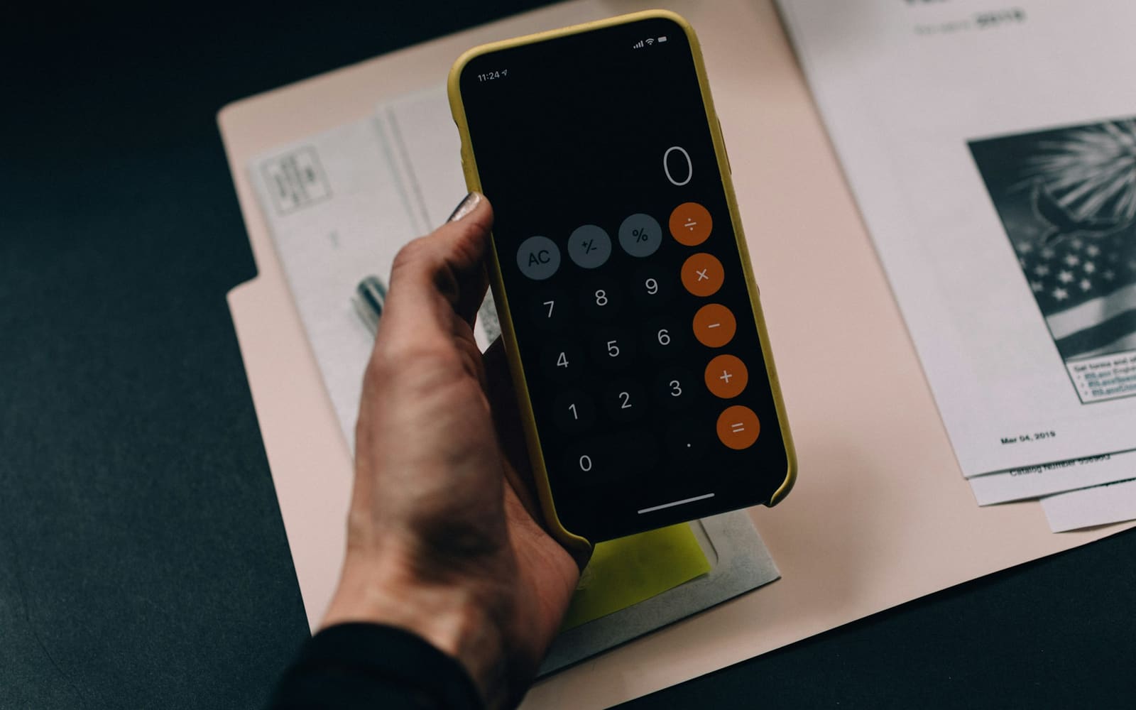 Pessoa usando a calculadora do celular sobre documentos financeiros